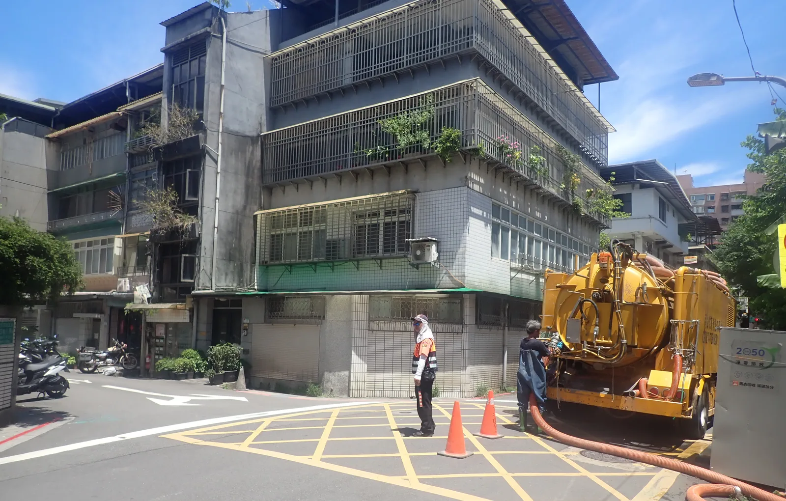 黃色清溝車停在路口的黃色網格線上,周圍擺著三角錐,師傅站在車尾拉出吸管