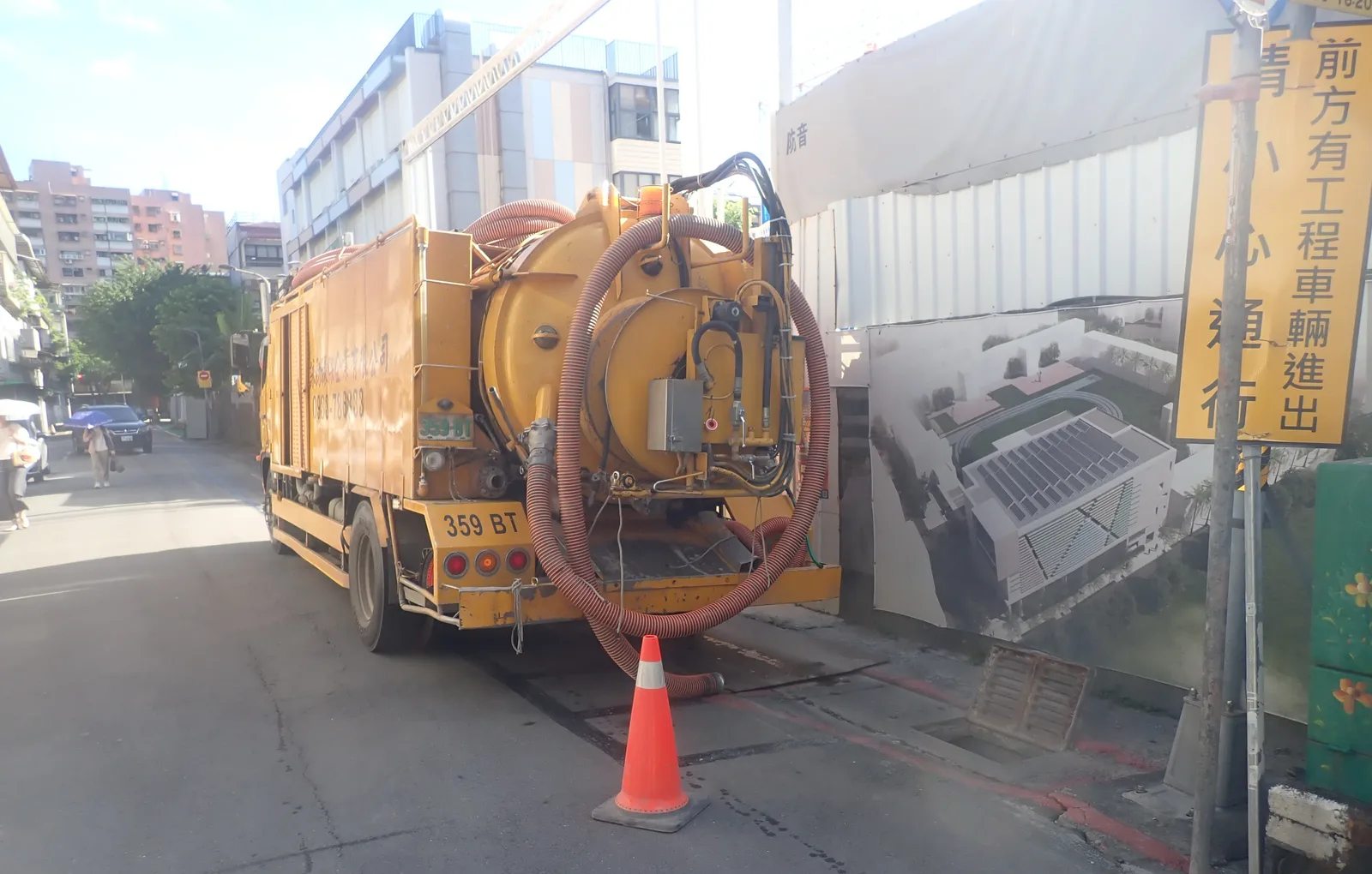 黃色清溝車停在工地圍籬旁，吸管垂到路邊，旁邊立著「前方有工程車輛進出」的告示