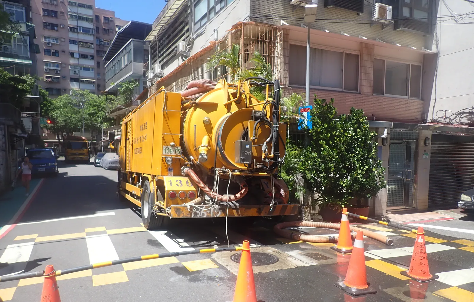 黃色清溝車停在巷口，前方一排三角錐，吸管拉進路面的人孔