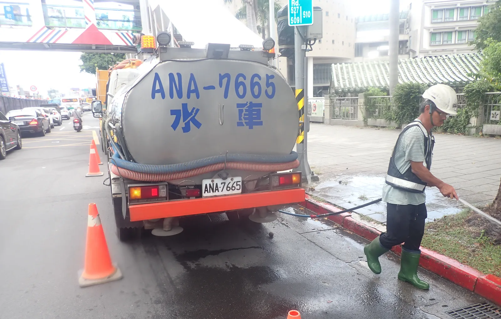 師傅在水車後方沖洗紅線旁的邊溝，路上擺著三角錐
