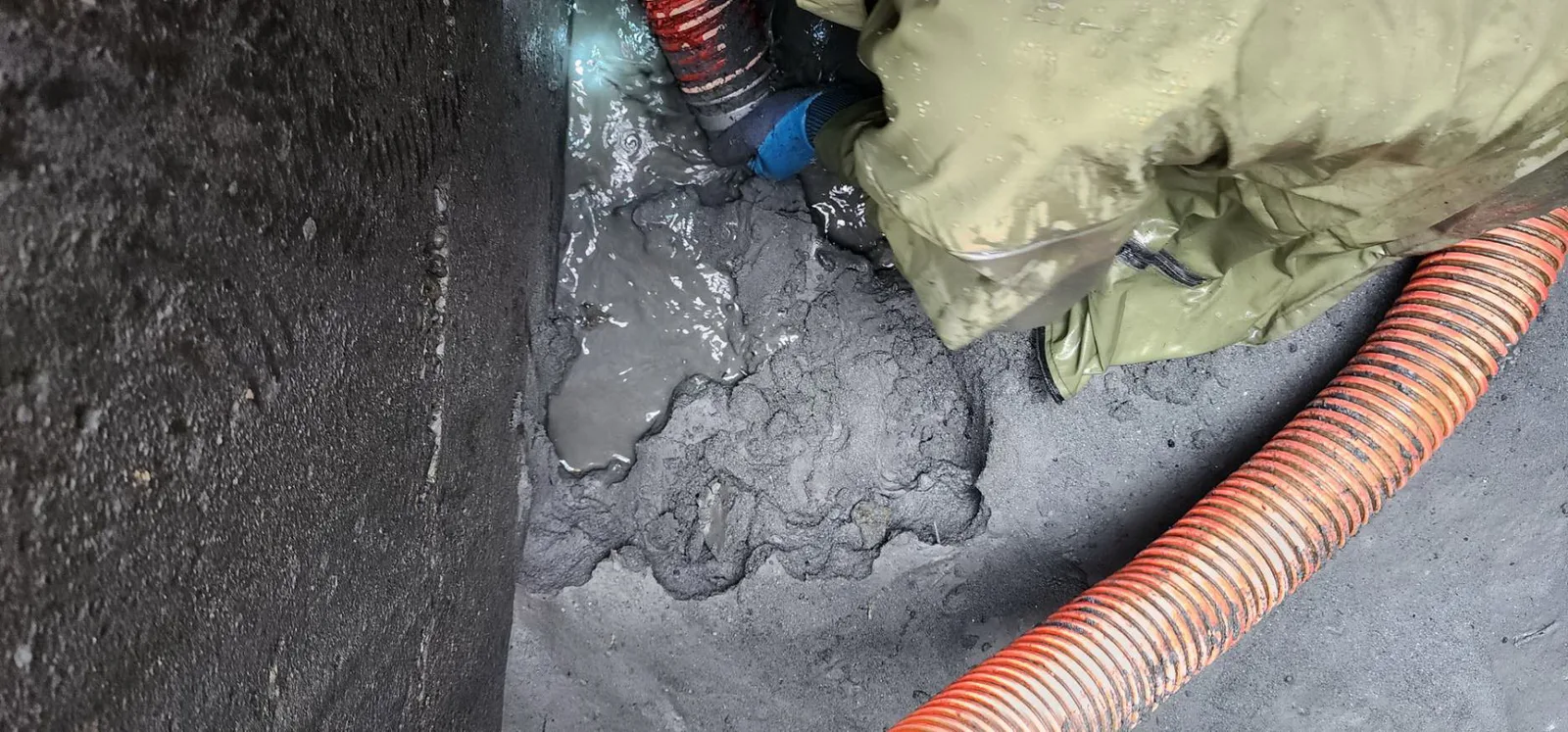 穿綠色雨衣的師傅蹲在溝內，用吸管抽除灰色泥漿