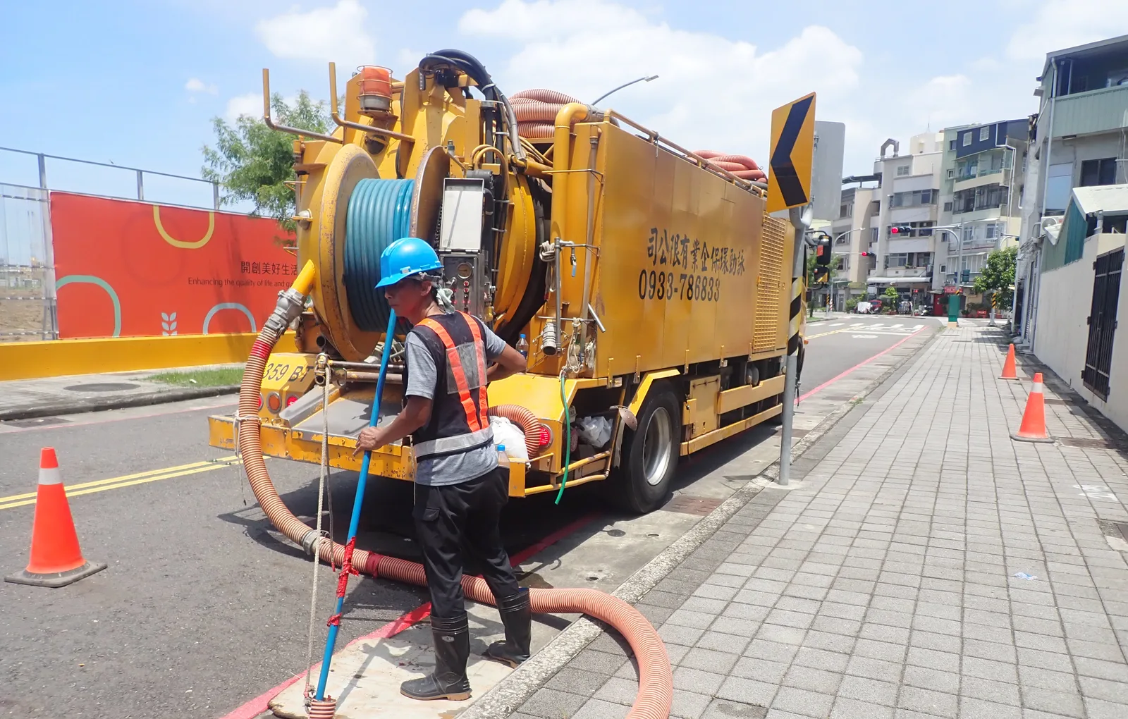 黃色清溝車停在路邊，戴藍色安全帽的師傅拉著抽吸管作業