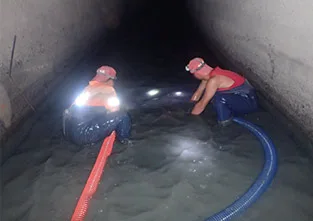 兩位戴頭燈的師傅在箱涵內的積水中作業